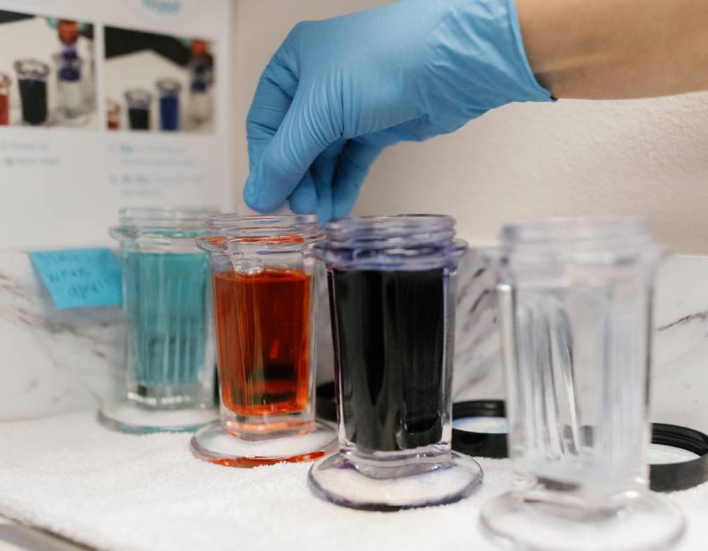 Woman in blue gloves handling colorful liquids in test tubes on a table